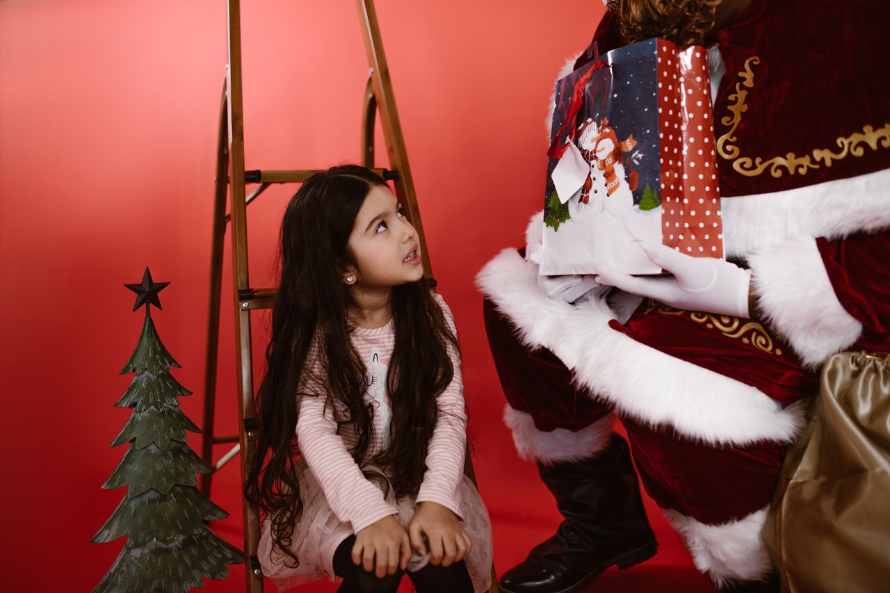 Young girl meeting Santa Claus with a Christmas gift indoors.